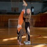 Two girls having fun practicing gymnastics in a sunny indoor sports hall.