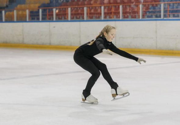 A young girl skillfully executing a figure skating move in an indoor ice rink.