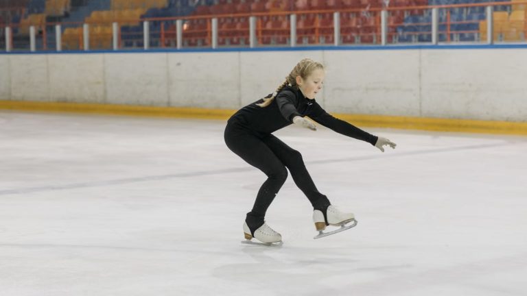A young girl skillfully executing a figure skating move in an indoor ice rink.